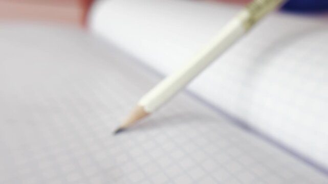 Close up of a wooden pencil drawing a line on a squared paper notebook, symbolizing creativity, education, writing, and the importance of note taking for ideas