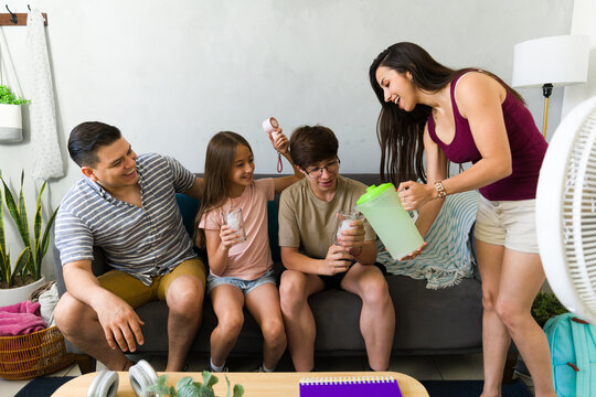 Cheerful family staying cool at home during summer, drinking refreshing lemonade, coping with hot weather