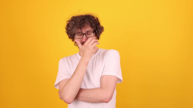 Person covering mouth with a hand in a bright yellow studio portrait, showing a mix of surprise, embarrassment and mild fear through a tense expressive gesture.
