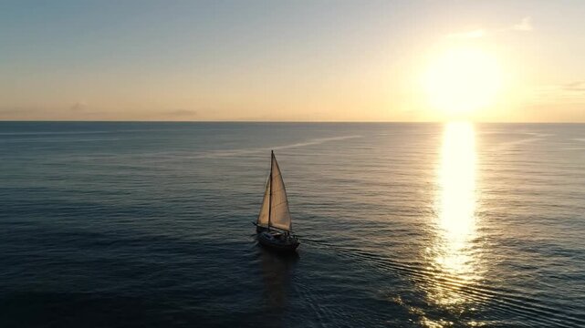 Aerial wide shot of a traditional wooden sailboat sailing across a calm ocean during sunset, featuring a bright golden sun reflection on the water and extensive negative space.