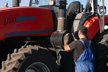 A tractor operator farmer takes out or installs an air filter in his tractor to clean, purge, or replace it. Maintenance of agricultural machinery in the field during sowing or harvesting. © Vladimir Razgulyaev