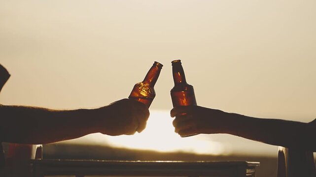 Man and woman toast with beer bottles, with a bottle placed on a table at sunset with an ocean view. A couple in love is relaxing at a seaside resort in sun beds and getting pleasure and relaxation 