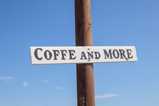 Wooden sign reading Coffee and More mounted on a pole against a clear blue sky.