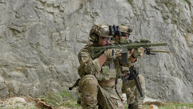 Special forces soldiers in full tactical gear on a military mission, securing a rocky perimeter while aiming their assault rifles in a coordinated team operation.