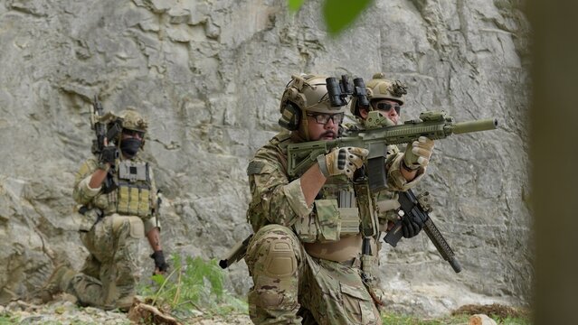 Special forces soldiers in full tactical gear on a military mission, securing a rocky perimeter while aiming their assault rifles in a coordinated team operation.