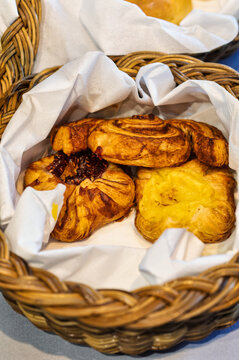 Danish pastries inside wicker basket on breakfast buffet table, served on white paper napkins