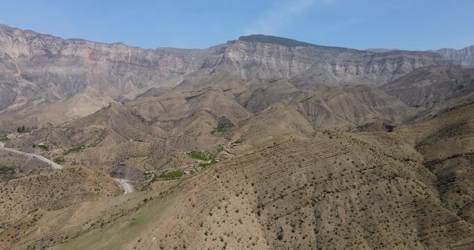 Cinematic aerial tracking shot of beautiful layered mountain slopes and winding road in Dagestan landscape