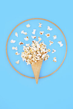 Abstract summer popcorn ice cream cone design with wooden frame on blue background. Surreal food art for fun bizarre composition for greeting card.