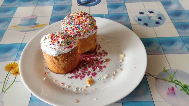 Two Easter cakes with sprinkles on a floral plate with crumbs and tea mug in background