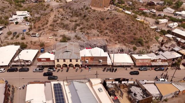 High-angle aerial flyover of historic Oatman, Arizona, a famous desert mountain town with cars parked along the main street.