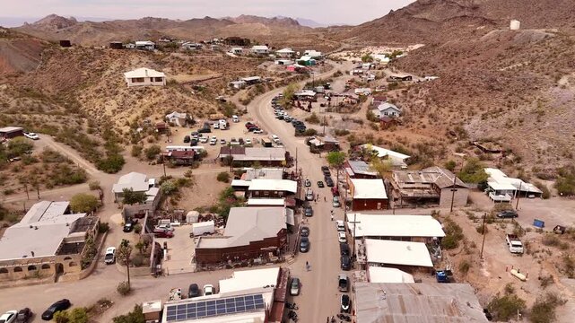 High-angle aerial flyover of historic Oatman, Arizona, a famous desert mountain town with cars parked along the main street.