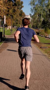 Athletic man jogs around a small lake in Los Angeles. Vertical video.