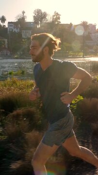 Athletic man jogs around a small lake in Los Angeles. Vertical video.