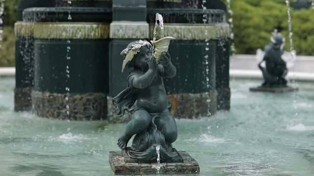 Close up of an ornamental fountain sculpture surrounded by flowing water in a landscaped park setting. Elegant outdoor architecture and tranquil atmosphere.