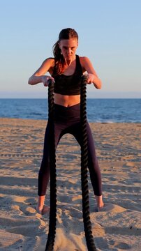 Attractive woman working out on the beach with battle ropes at sunset. Slow Motion. Vertical video.
