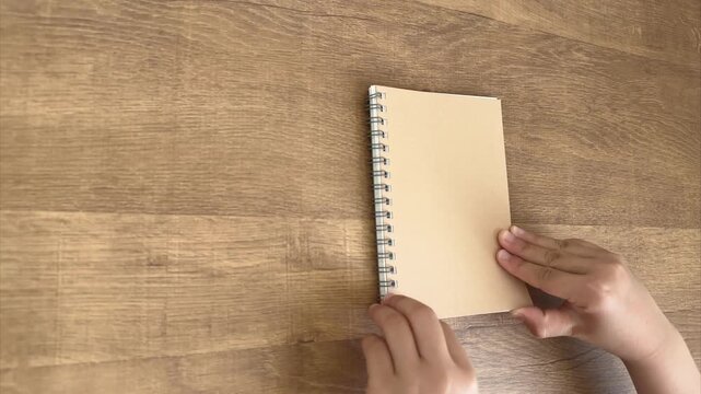 Child Hands Opening a Small Spiral Notebook from an Oblique Overhead View, 4K Silent Video