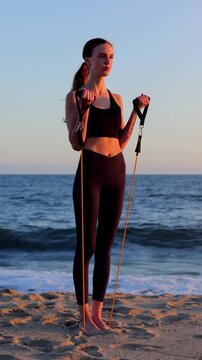 Attractive woman working out on the beach with resistance bands at sunset. Slow Motion. Vertical video.