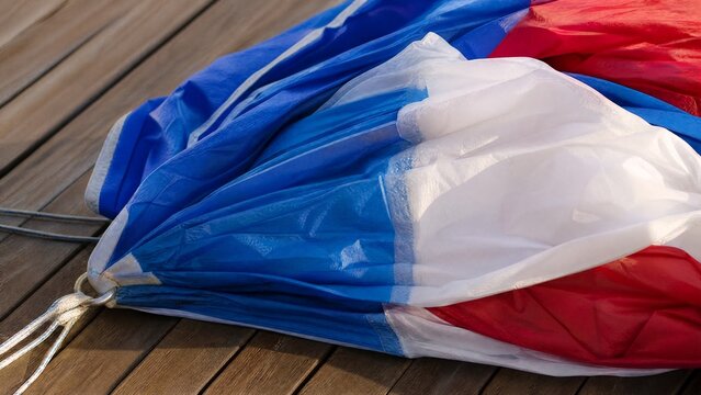 Folded nylon spinnaker sail on wooden deck, colorful textures.