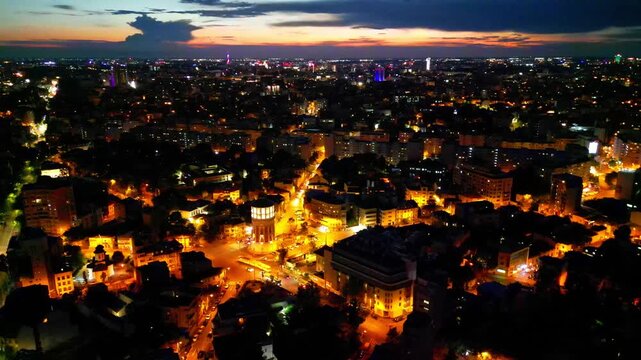 Cinematic high angle night view of the illuminated Bucharest fire tower in Romania. Iconic historic brick landmark surrounded by glowing city lights.
