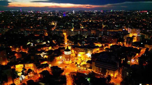 Cinematic high angle night view of the illuminated Bucharest fire tower in Romania. Iconic historic brick landmark surrounded by glowing city lights.