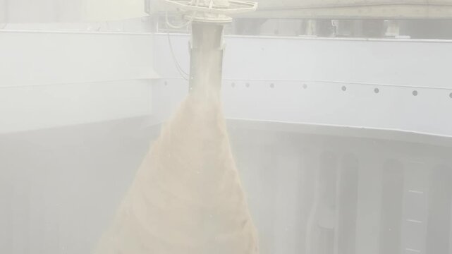 Bulk wheat loading at seaport. Continuous stream of grain from pipe to ship hold with dense dust clouds. Global commodity export and logistics.