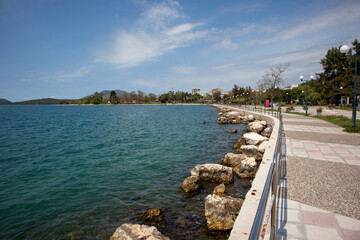 Obraz premium Seaside promenade with rocky shoreline and calm sea water under blue sky in Igoumenitsa, Greece.