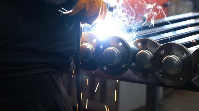 Close-up of welding stainless steel pipe flanges, bright arc and sparks in industrial workshop, 4K