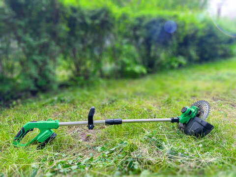 Cordless electric brush cutter with metal blade on freshly cut grass in backyard garden maintenance