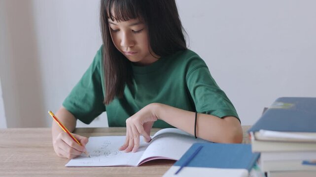 Selective focus portrait of an Asian kid improving her writing skills. The young student is focused on her textbook assignment, representing homeschooling, diligent study, and modern education.