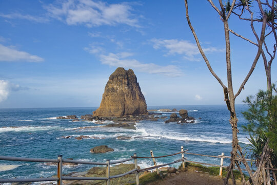 Beautiful viewpoint overlooking the grand sea stack at Papuma beach with a wooden safety fence and pandan trees, Jember, East Java, Indonesia.