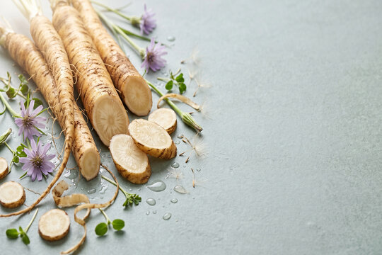Raw salsify root vegetables with cut slices, purple flowers, and microgreens on a light gray background