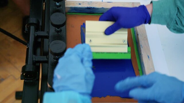 Worker using a squeegee to spread ink across a screen printing frame during textile production