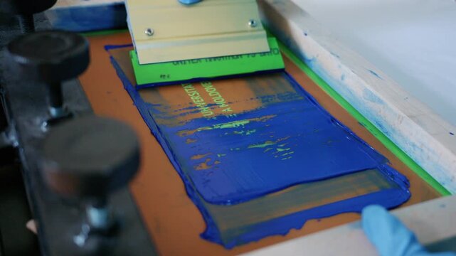 Worker using a squeegee to spread ink across a screen printing frame during textile production