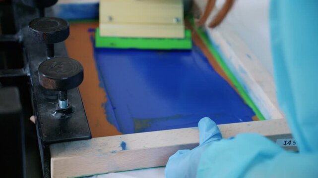 Worker using a squeegee to spread ink across a screen printing frame during textile production