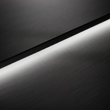 A diagonal close-up of a brushed black metal surface with a bright line of light reflecting off the metallic texture.