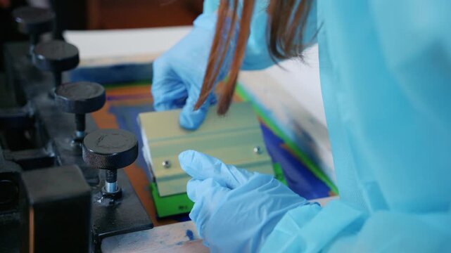 Worker using a squeegee to spread ink across a screen printing frame during textile production