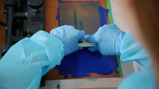 Worker using a squeegee to spread ink across a screen printing frame during textile production