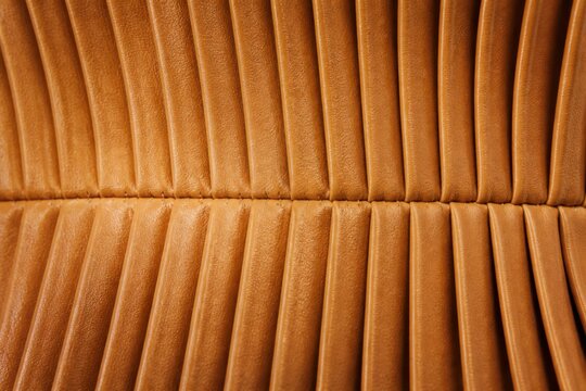 Close up of brown leather car seat upholstery with stitched pleats and warm textured interior detail