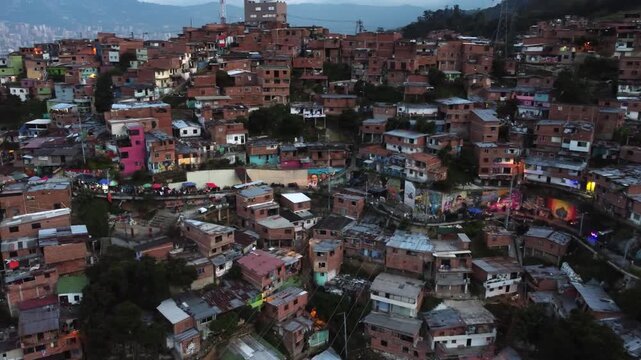Panning close up aerial hillside view of the Comuna 13 neighborhood and pedestrian walkway, in Medellin, Colombia at dusk with Medellin skyline in background