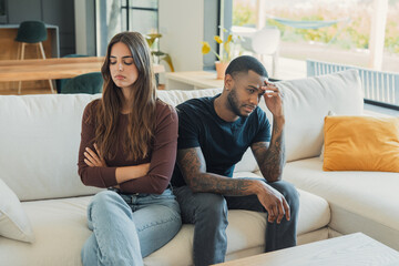 Obraz premium Frustrated woman sitting with crossed arms next to a stressed man on a sofa, both feeling distant and upset after an argument and dealing with communication breakdown