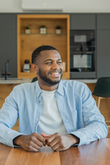 Fototapeta premium Young black man smiling and looking away while sitting at a kitchen island, representing concepts of domestic life, happiness, and well-being in a contemporary home environment
