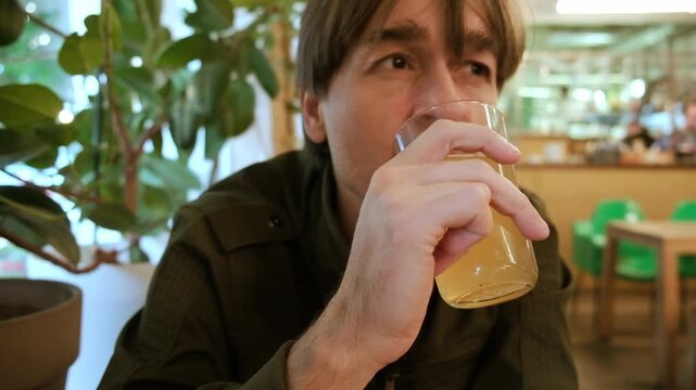 Close-up shot of a man drinking a glass of hazy craft beer or juice in a cafe horizontal view
