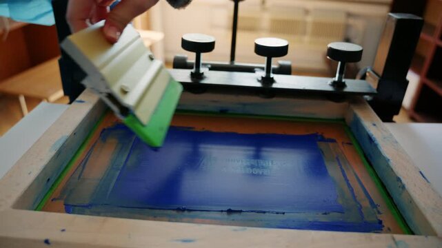 Worker using a squeegee to spread ink across a screen printing frame during textile production