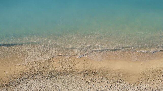 Sea waves gently meeting the sandy beach in a tranquil aerial top down view