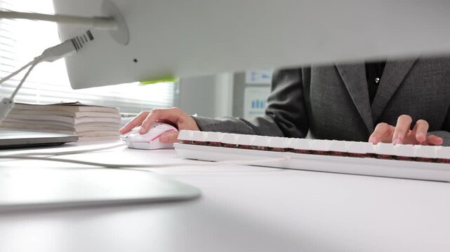 Corporate professional working in a modern office, typing on a keyboard and using a computer mouse. Close-up view of employee hands at work.