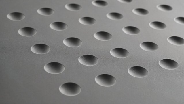 Grid of circular indentations on gray surface with side lighting.