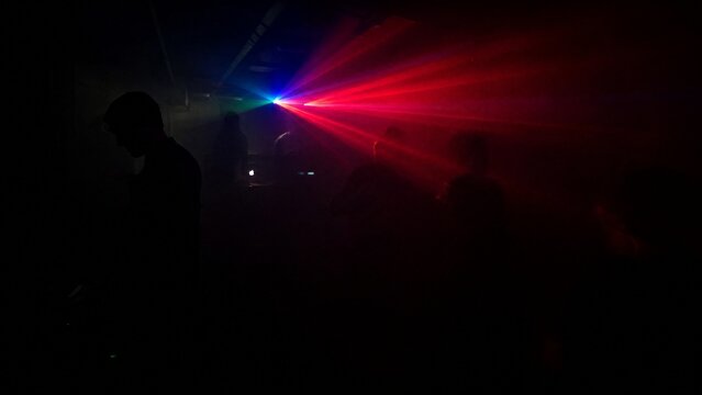 Dark underground club with single colorful laser beam through haze.