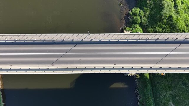 Top down aerial view of a white car driving along a modern concrete bridge over a river. Minimalist highway road infrastructure design at sunny day.