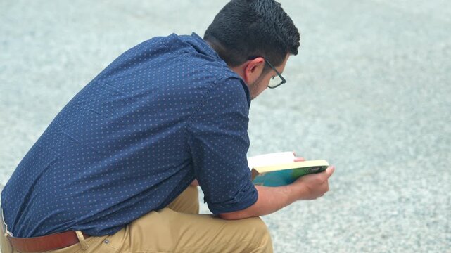 A man reads a book while sitting in a public plaza in Chicago. The scene shows concentration and quiet moments in a busy urban environment.
