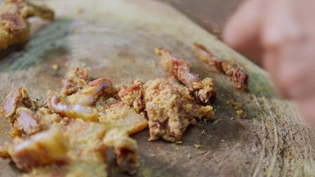 Close-up of a chef chopping crispy fried pork with a large cleaver on a rustic wooden board, preparing an authentic Asian street food dish for serving.